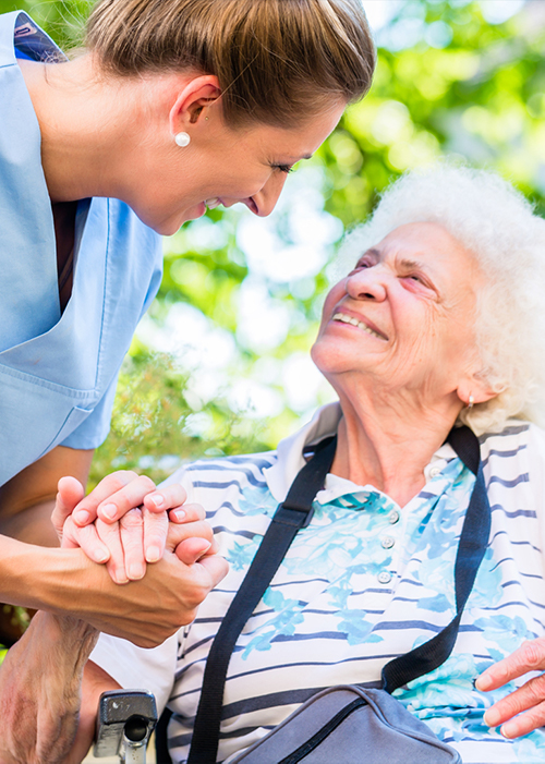 Smiling elderly woman sitting and looking up to carer while holding her hand